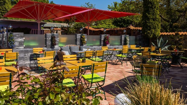 An outdoor patio with yellow and green seating, red umbrellas, and potted plants. - Kos - sparrow lust - sparrow lust (Koserow)