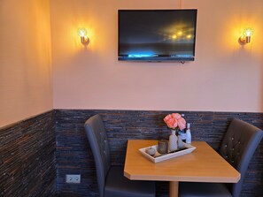 A corner booth with a TV mounted on the wall, two wall sconces, a table with a tray of items, and a stone accent wall.
