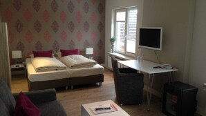 A hotel room with a bed, a desk, a television, a small table, and a couch. - Superior double room - Hotel Insel Pension (Niebüll)