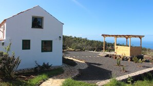 A white building with green shutters, a stone pathway, and a pergola with a wooden frame.