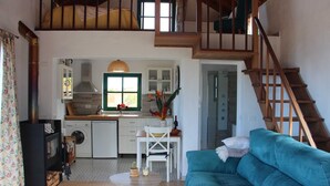 A cozy living room with a blue sofa, a wooden staircase, a kitchen with a washing machine, and a dining area with a table and chairs.
