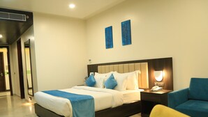 A modern hotel room with a large bed, bedside tables, a chair, and artwork on the wall.