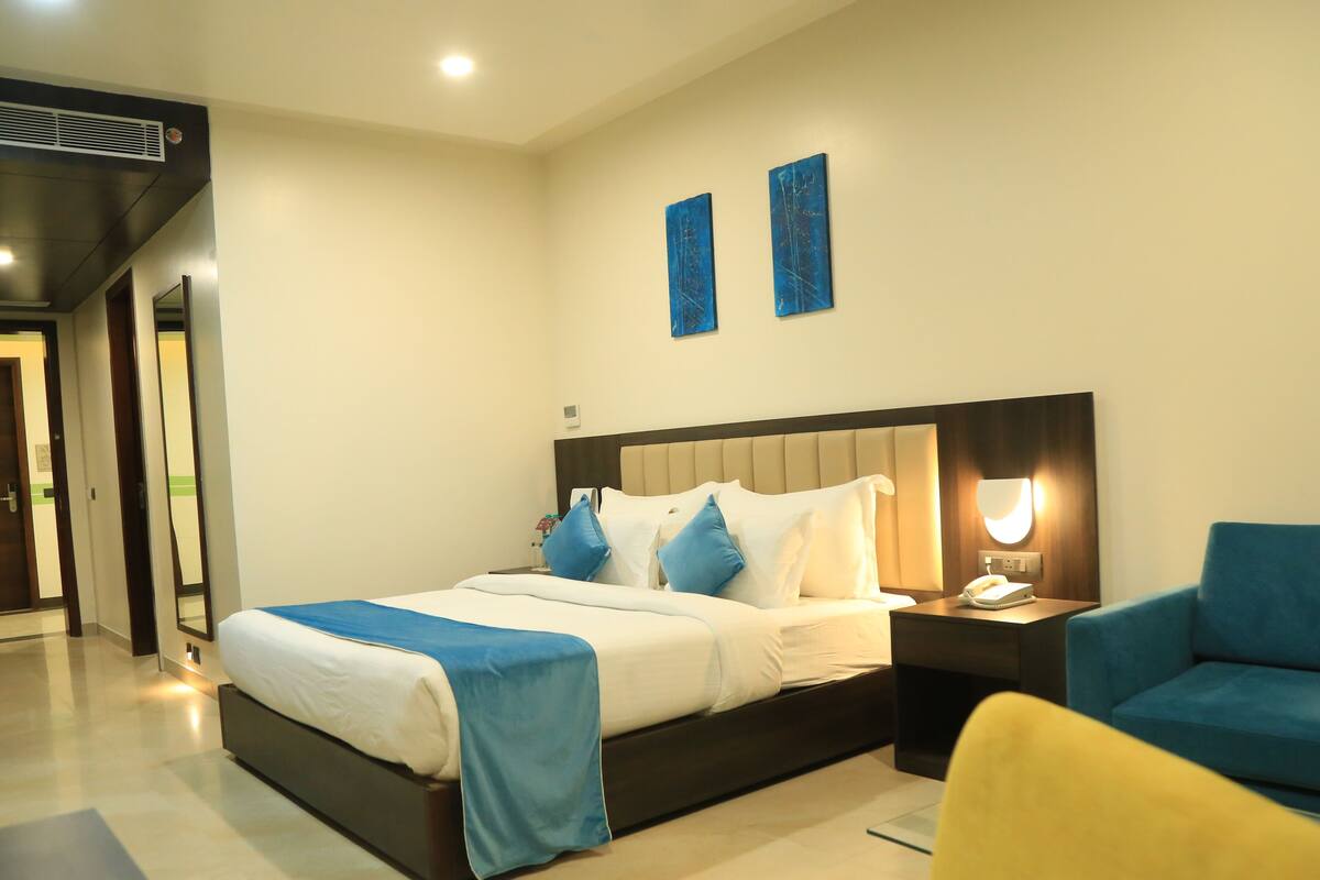 Quarto de hotel moderno com uma cama grande, mesas de cabeceira, uma cadeira e obras de arte na parede.