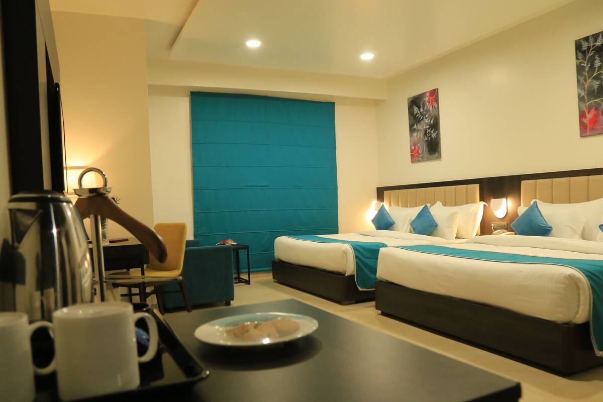 Quarto de hotel com duas camas, uma escrivaninha com cafeteira e uma cadeira.