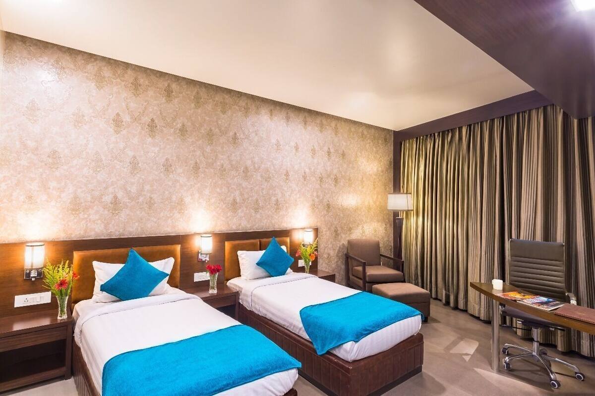 Quarto de hotel com duas camas, uma escrivaninha, uma cadeira e uma televisão.