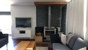 A modern living room with a flat-screen TV, a wooden coffee table, a gray sofa with striped pillows, and a stone fireplace. - Huge House Fantastic for Families and friends (Anglers Reach)