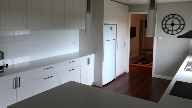 A modern kitchen with white cabinetry, a built-in refrigerator, pendant lights, and a clock on the wall. - Huge House Fantastic for Families and friends (Anglers Reach)