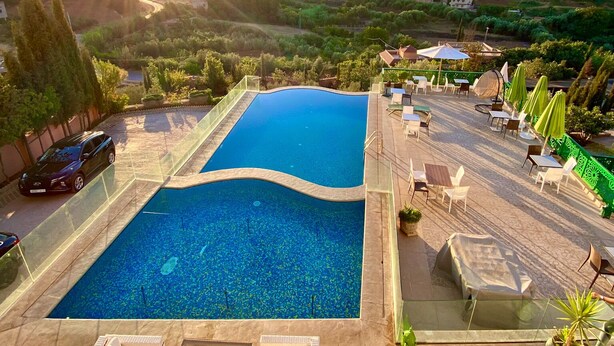 A swimming pool with lounge chairs and tables, surrounded by a patio area with a view of a hilly landscape. - Dar Zayane (Mouha ou Hammou Zayani)