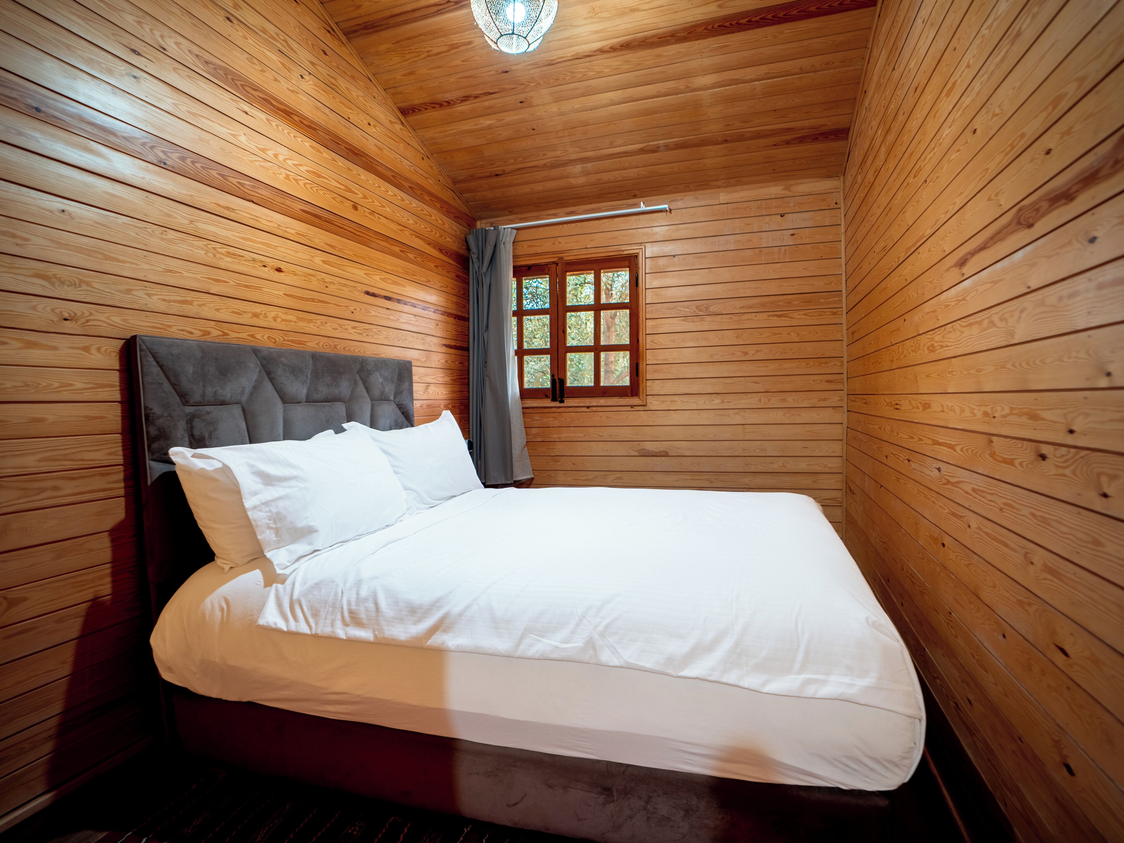 Una habitación de cabaña de madera con cama, ventana y luz de techo.
