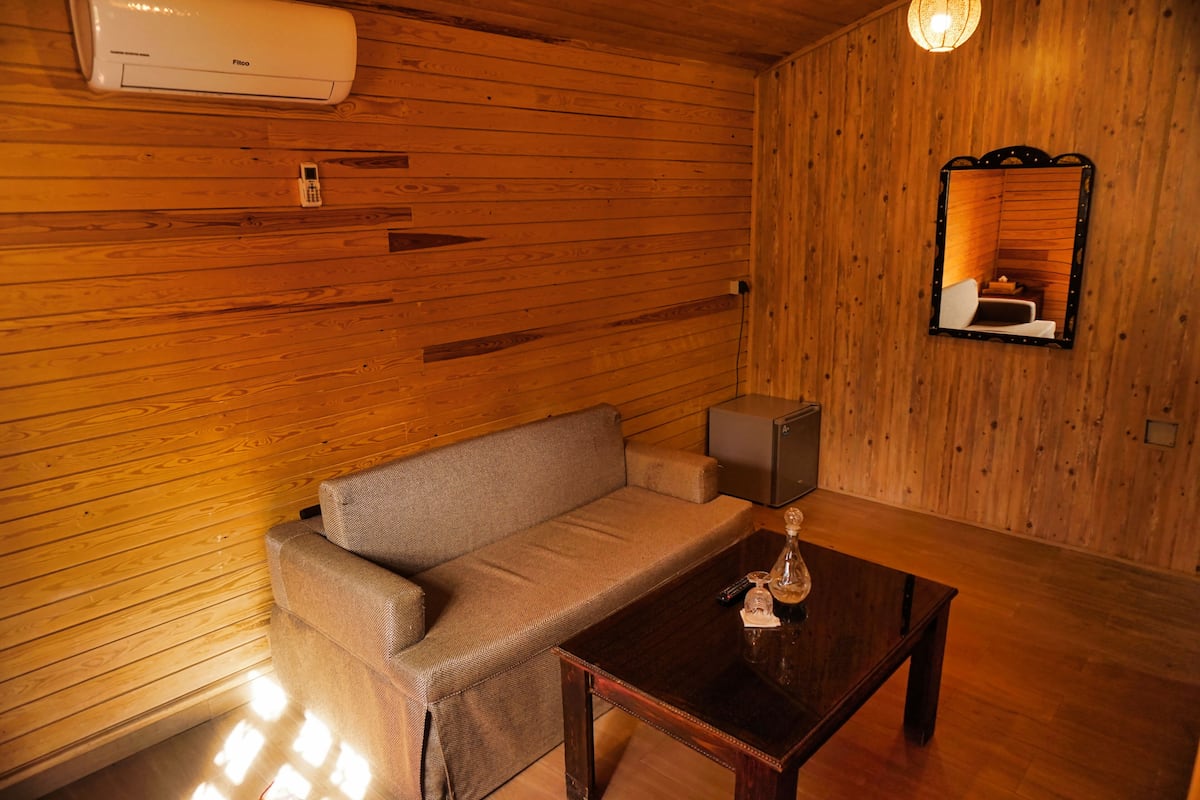 A wooden-paneled room with a sofa, a coffee table, a lamp, and a mirror.