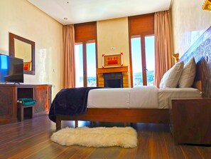 A bedroom with a bed, a television on a wooden cabinet, a fireplace, and a view of the outdoors. - Dar Zayane (Mouha ou Hammou Zayani)