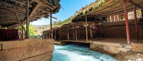 A traditional wooden structure with a thatched roof over a river.