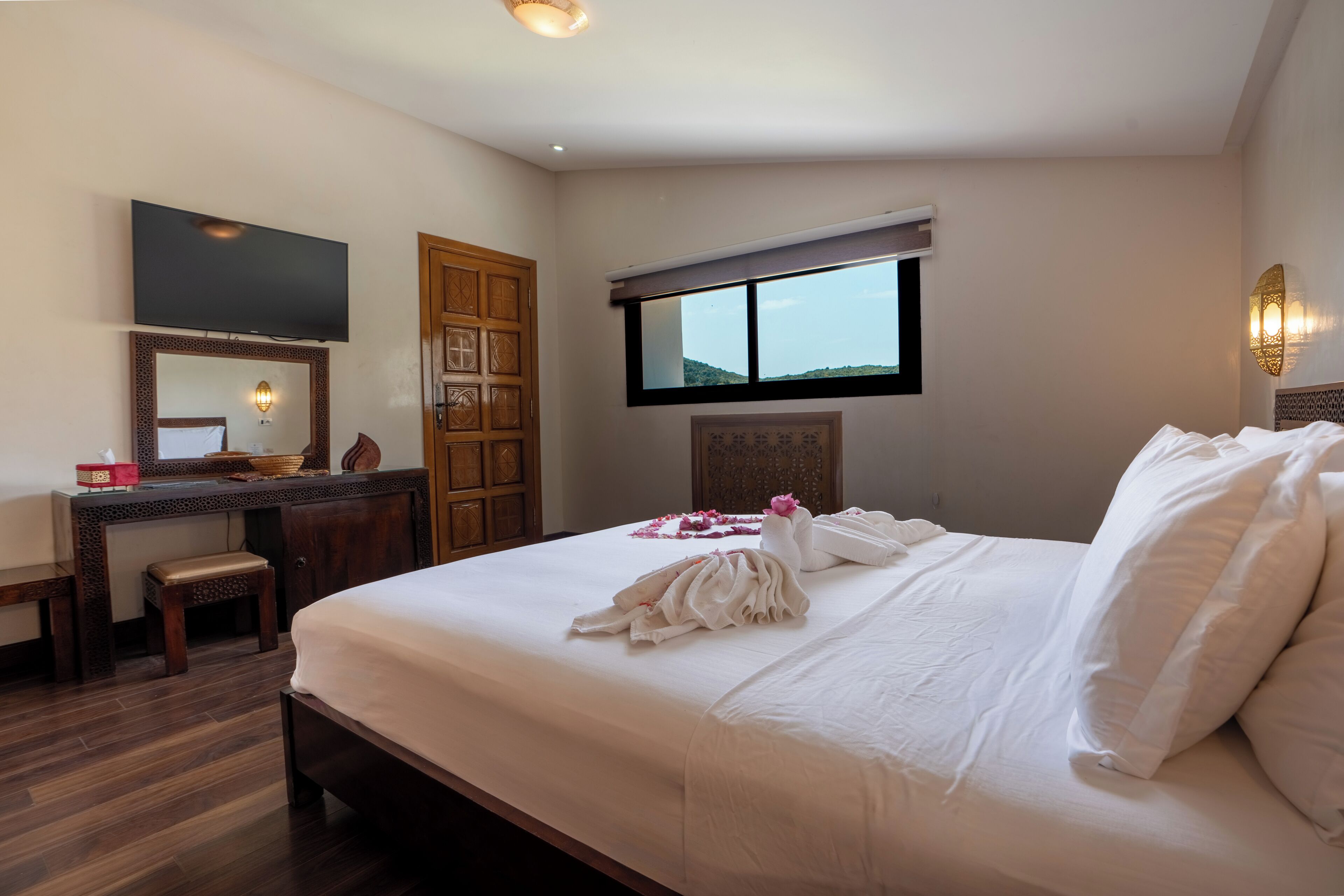 A hotel room with a bed, a desk, a television, a window, and a door.