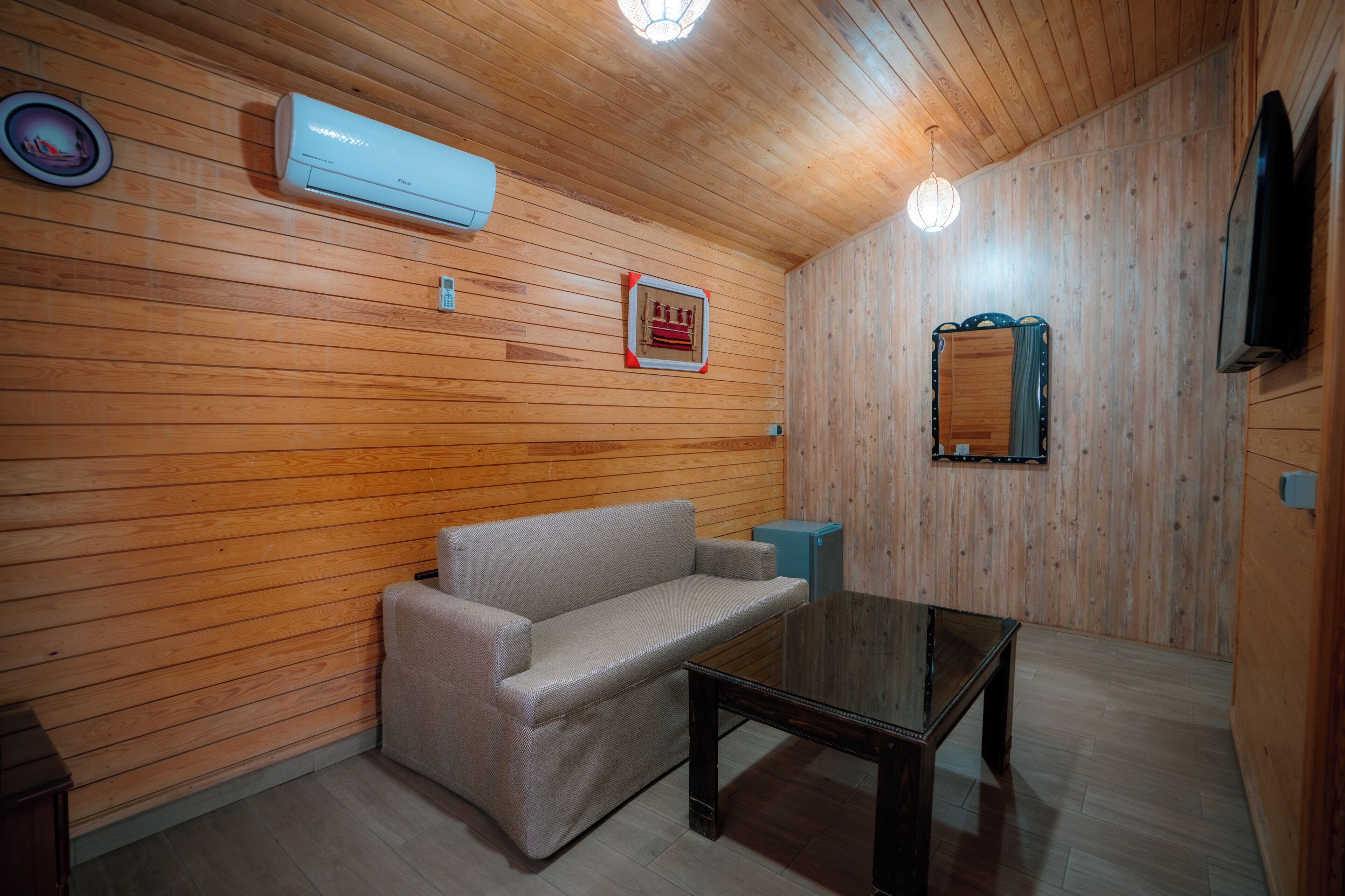 A room with wooden paneling, a sofa, a table, an air conditioning unit, and a television.