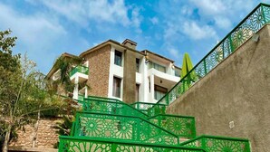 A modern building with a stone facade, a green metal staircase with intricate designs, and a clear blue sky. - Dar Zayane (Mouha ou Hammou Zayani)