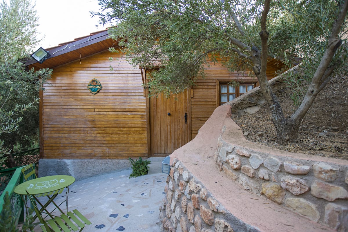 Eine Holzhütte mit einer Steismauer, einer Holztür und einer kleinen Terrasse mit Tisch und Stühlen.