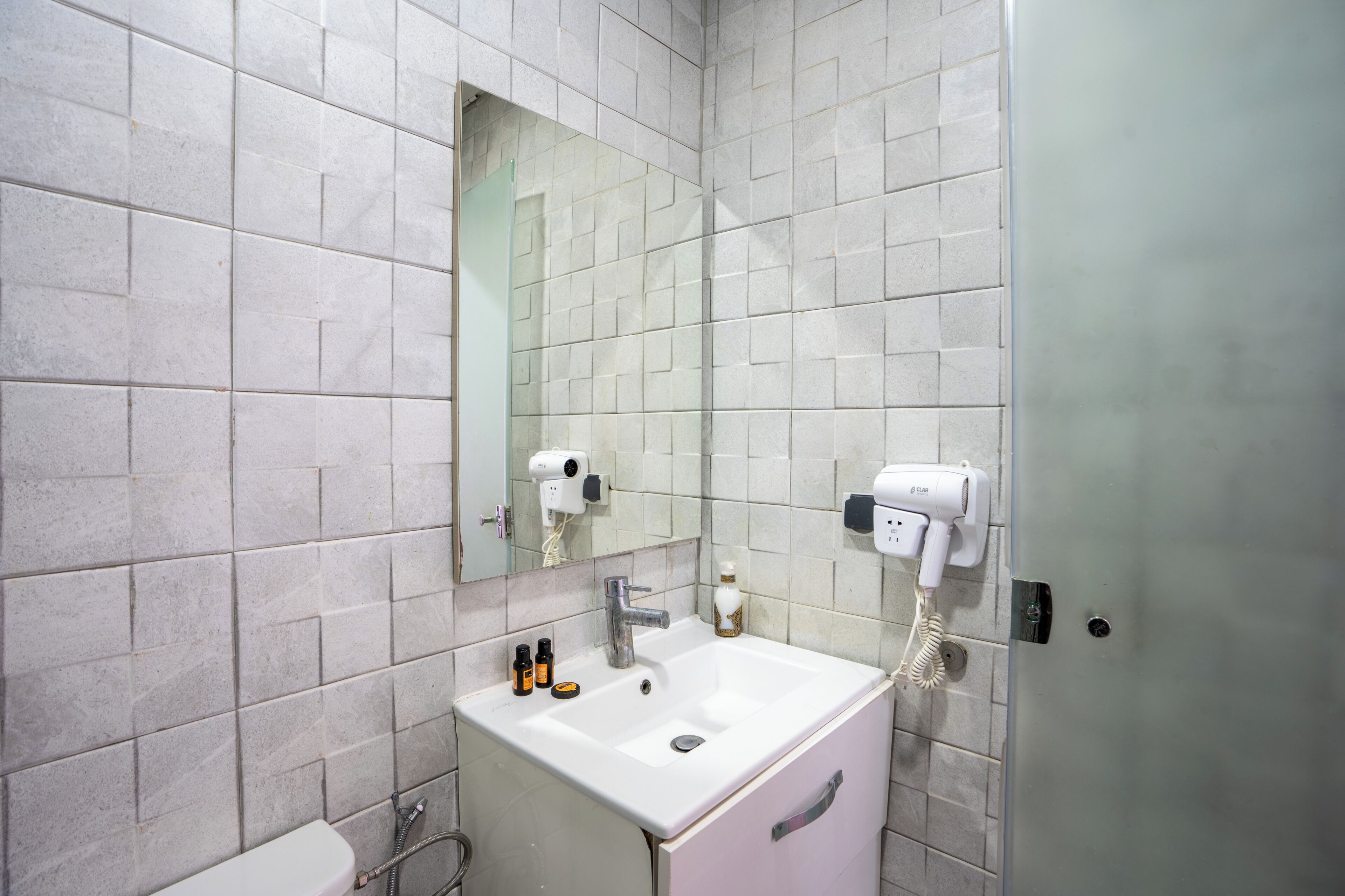 A bathroom with a white sink, a mirror, and a hairdryer mounted on the wall.