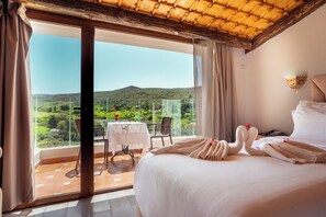 A hotel room with a bed, a table with a vase, and a view of a green landscape through a glass door.