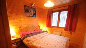Un dormitorio rústico de madera con una cama, mesitas de noche, una lámpara y una ventana con cortinas.