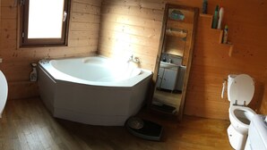 Un baño de cabaña de madera con bañera, inodoro, lavamanos y ventana.