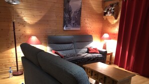 Una habitación acogedora con un sofá gris, una mesita de madera, dos lámparas rojas y un cartel en la pared.