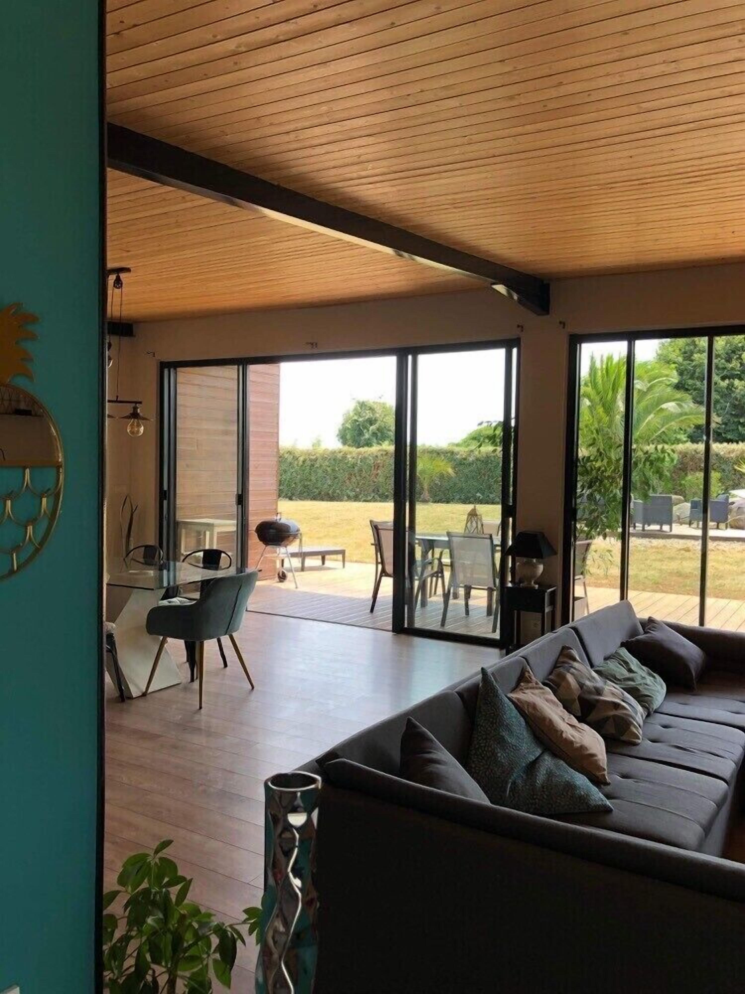 A modern living room with a large sofa, a dining area with a table and chairs, and a view of a garden through large windows.