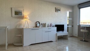 En moderne stue med et hvidt skab, et fjernsyn, en lampe og et lille bord.