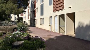 En bygning med flere etager, en asfalteret indkørsel, en bil parkeret til siden, og en have med forskellige planter og blomster.
