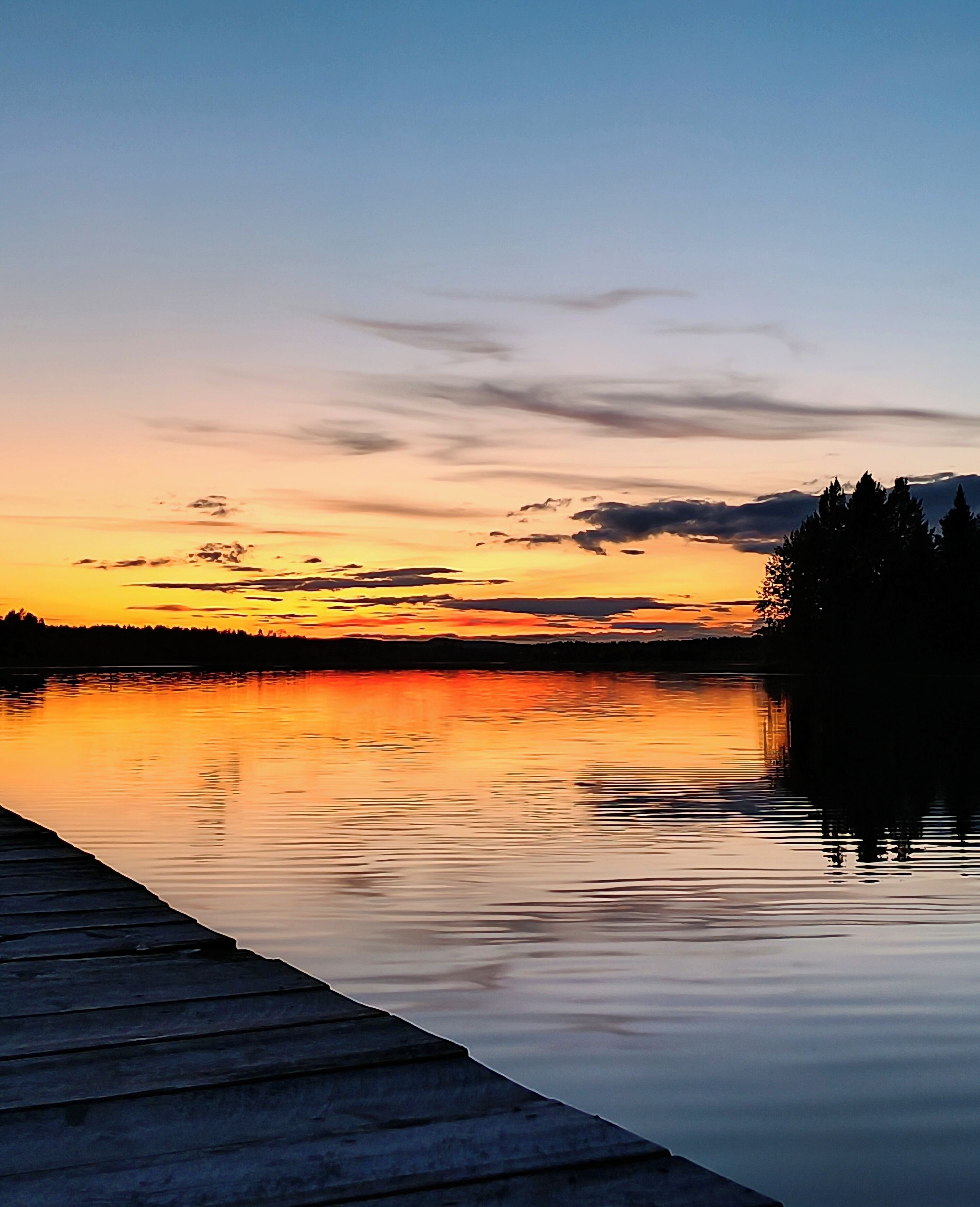 A calm lake at sunset with a wooden dock extending into the water.