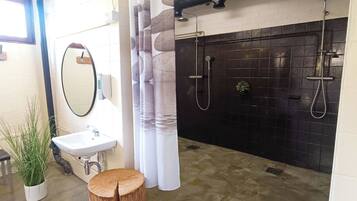 A bathroom with a sink, mirror, potted plant, wooden stool, and a black tiled shower area.