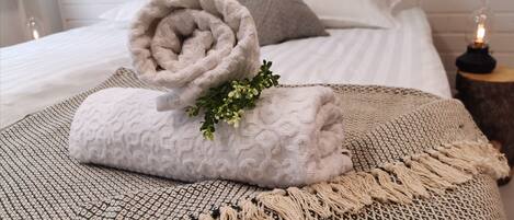 A neatly made bed with a rolled towel, a decorative plant, and a textured throw blanket.