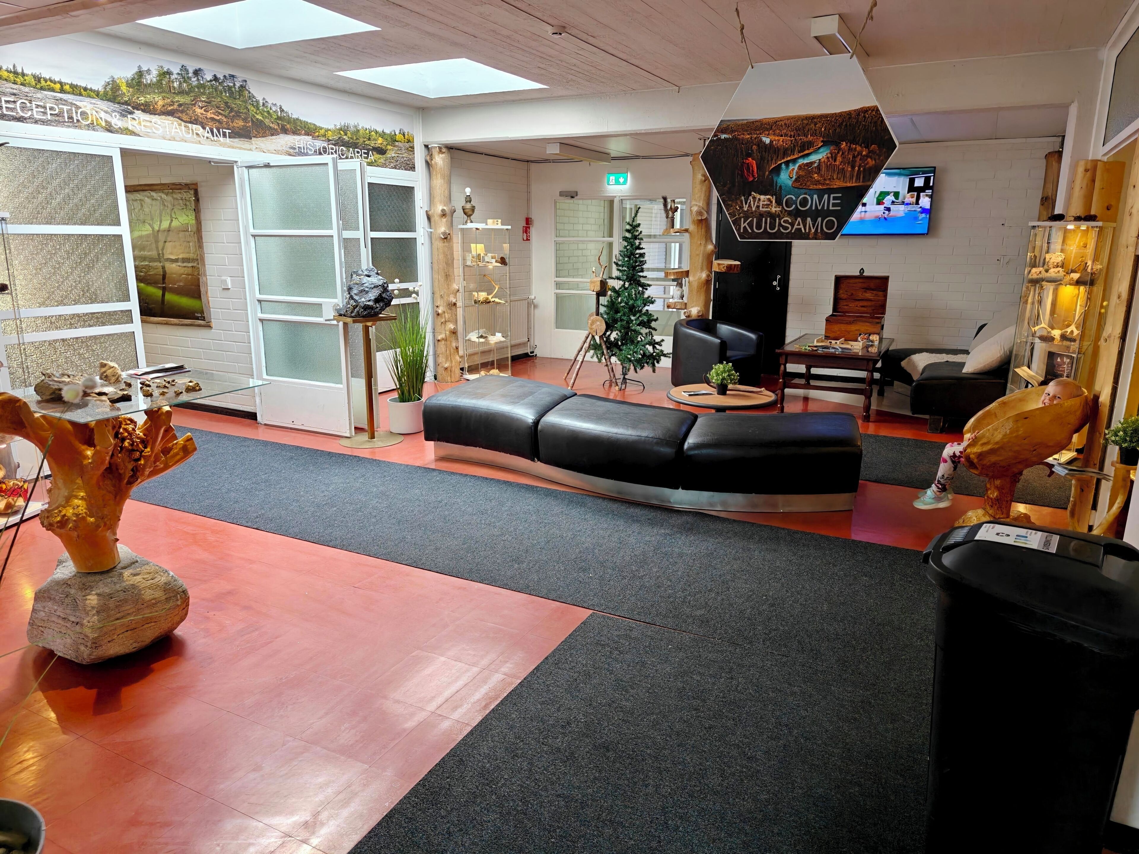 A reception area with a black leather sofa, a reception desk, a welcome sign, and a television screen.