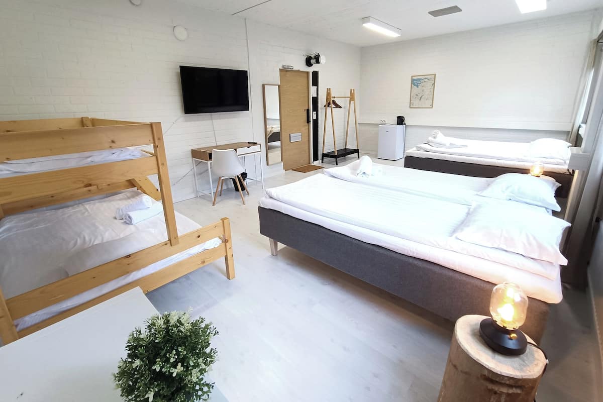A hotel room with bunk beds, a desk, a chair, a television, a mirror, a small refrigerator, and a bedside lamp.
