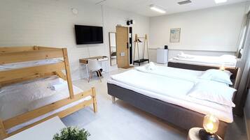 Une chambre d’hôtel avec des lits superposés, un bureau, une chaise, une télévision, un miroir, un petit réfrigérateur et une lampe de chevet.