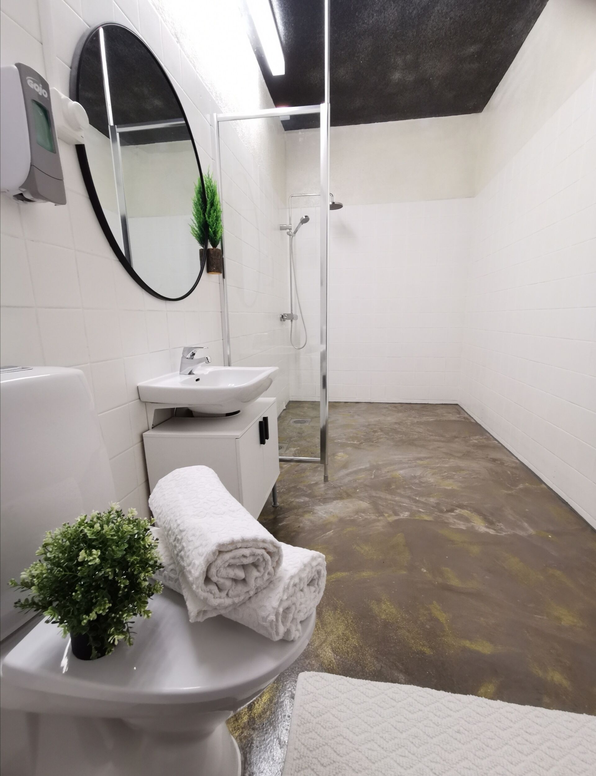 A modern bathroom with a white sink, mirror, and toilet. There is a shower area with a glass door and a towel on the floor.