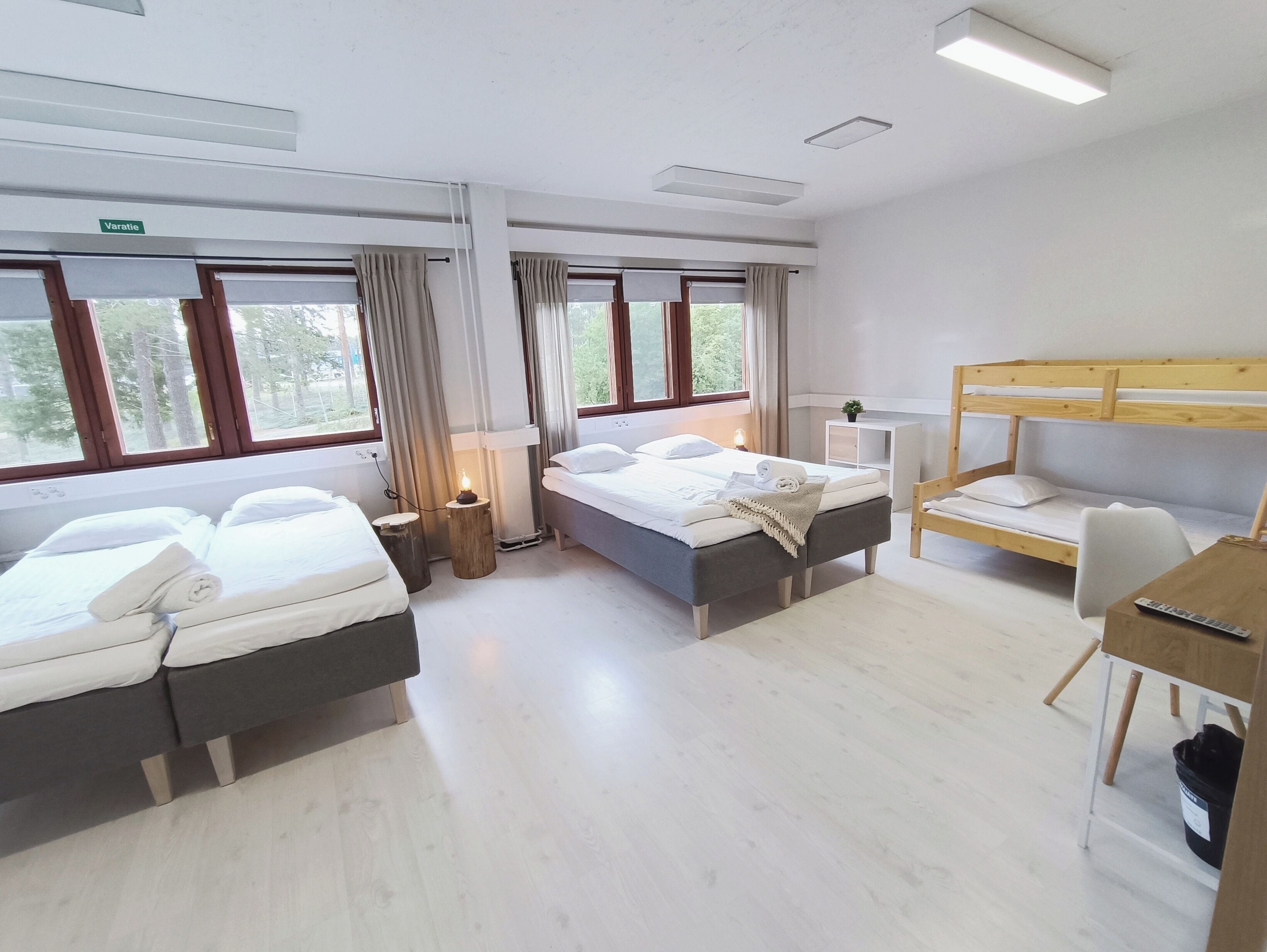 Habitación de hotel con dos camas, un escritorio, una silla, una mesita y una lámpara de noche.