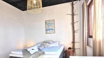 A bedroom with a bed, a hanging light fixture, a window with curtains, and a plant.