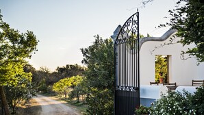 Un chemin pavé de pierres mène à une entrée fermée par un portail, devant laquelle se trouve un bâtiment blanc et une table entourée de chaises.