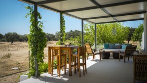 Une terrasse extérieure couverte, avec une table et des chaises en bois, un canapé et une vue sur un vignoble.