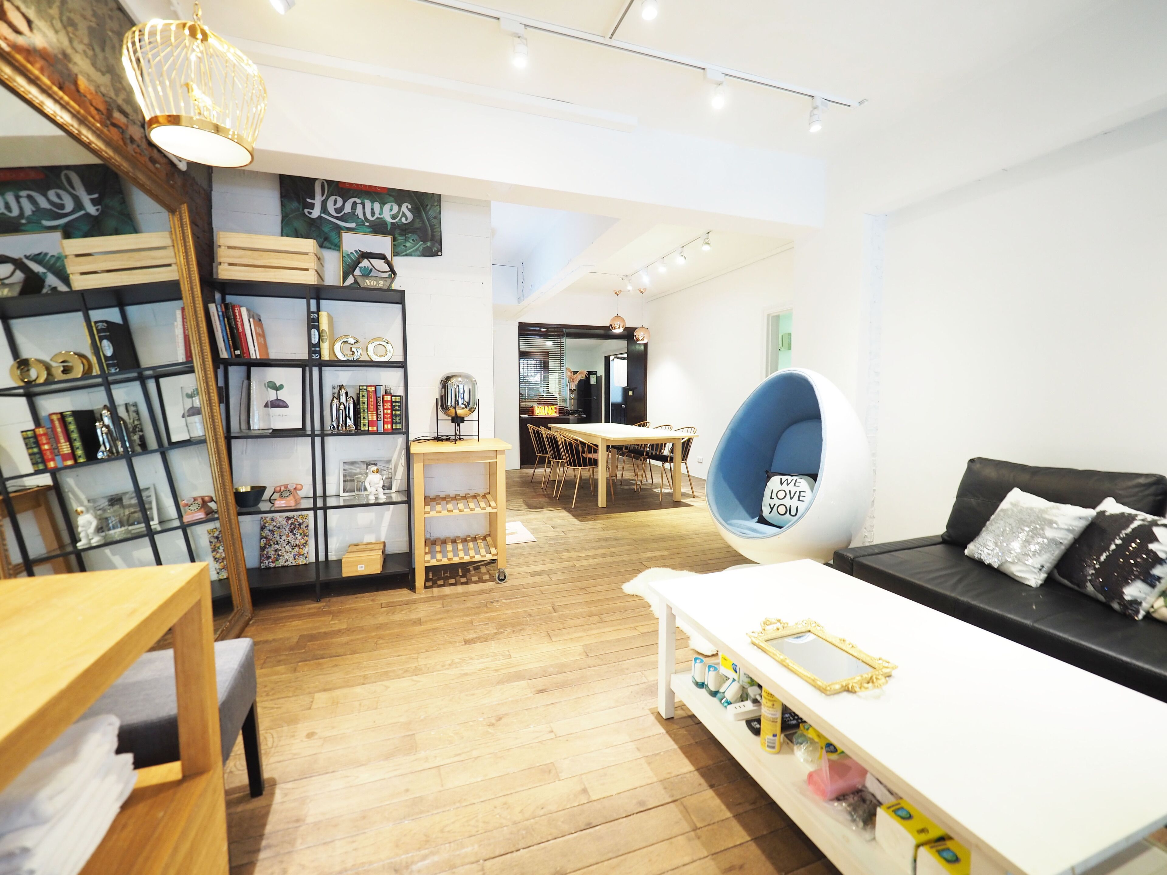 A modern living room with a white sofa, a wooden coffee table, a hanging chair, and a bookshelf filled with books and decorative items.