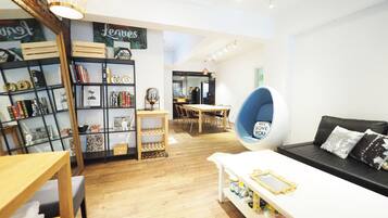 A modern living room with a white sofa, a wooden coffee table, a hanging chair, and a bookshelf filled with books and decorative items.