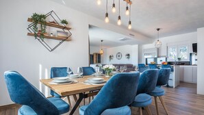 A modern dining area with a wooden table, blue upholstered chairs, and a kitchen in the background. - Beautiful home in Vrsi (Vrsi)