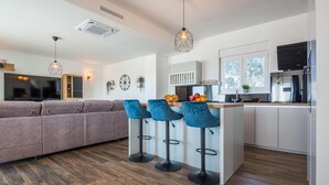 A modern kitchen with a central island, bar stools, and a grey sofa in a living area. - Beautiful home in Vrsi (Vrsi)