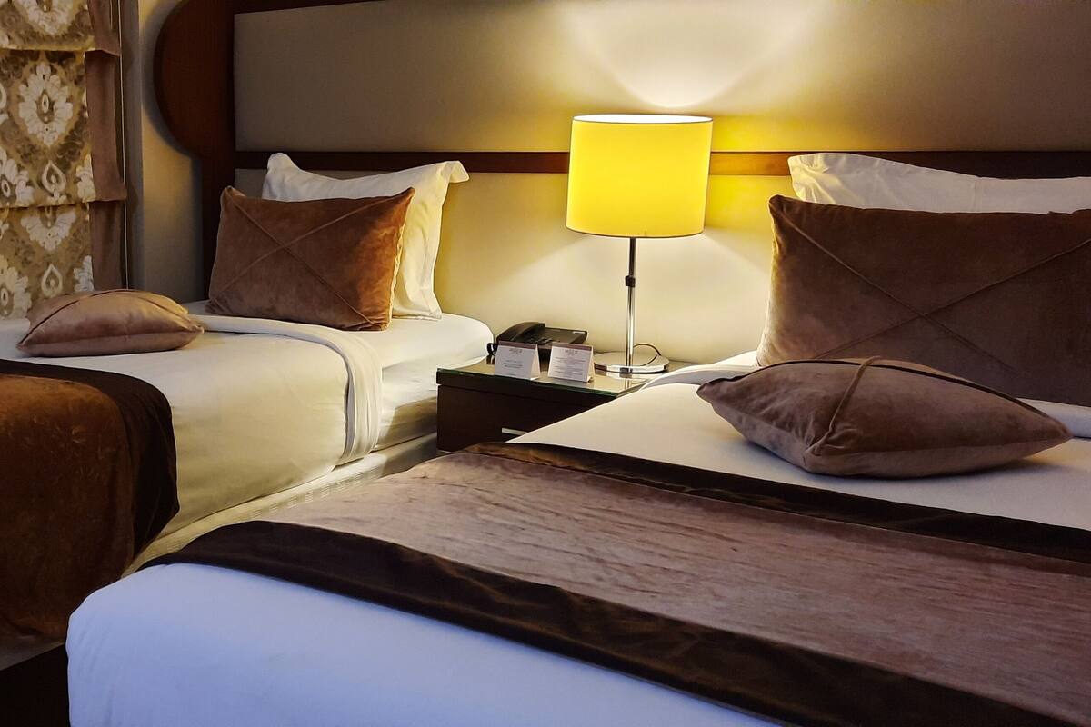 A hotel room with two beds, a nightstand with a lamp, and a patterned curtain.