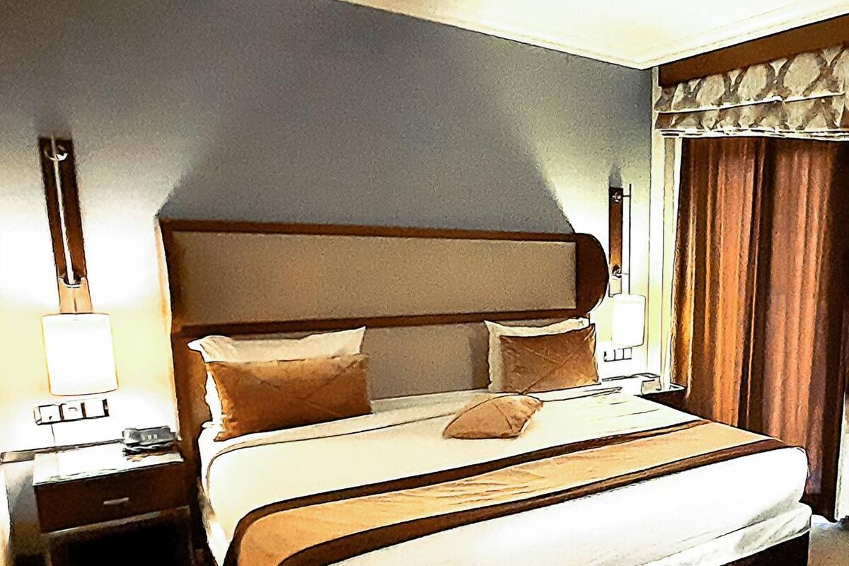 A hotel room with a large bed, a nightstand, a lamp, and a window with curtains.