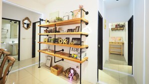 Ein modernes Interieur mit einer Holzregalanlage, die verschiedene Gegenstände zeigt, einer weißen Tür mit digitaler Uhr und einem Blick in ein Badezimmer mit Spiegel und Waschbecken.