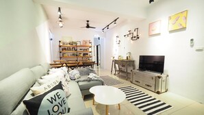 Ein modernes Wohnzimmer mit einem grauen Sofa, einem weißen Couchtisch, einem Fernseher auf einer Holzkommode und einem Bücherregal im Hintergrund.