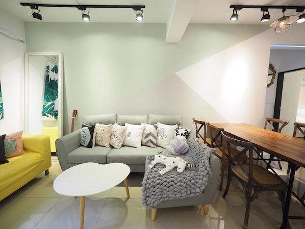 Una sala moderna con un sofá gris, una mesa de centro blanca, una mesa de comedor de madera y un sillón amarillo.