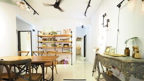Ein Essbereich mit einem Holztisch und Stühlen, einem schwarz-weißen Teppich und einem Bücherregal voller verschiedener Gegenstände.
