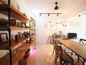 Una sala moderna con una mesa de comedor de madera, sillas, un televisor y un estante decorativo con diversos objetos.